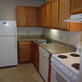 A compact kitchen with wooden cabinets, a refrigerator, electric stove, dishwasher, and a sink.