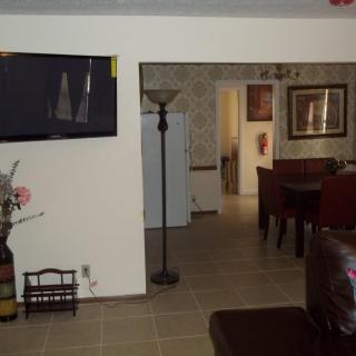 A cozy living room with a mounted TV, floor lamp, and dining area in the background.