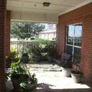 A cozy porch area with potted plants and a bench against a brick wall.