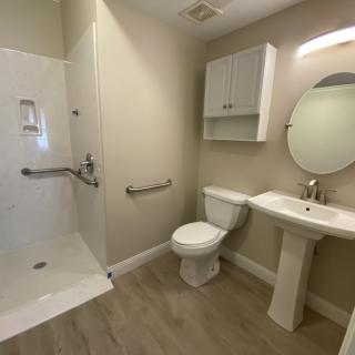 A modern accessible bathroom with a shower, toilet, and pedestal sink.