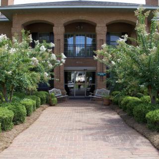 A brick pathway leading to a building's entrance, surrounded by lush greenery.