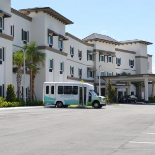 A small shuttle bus parked outside a large building with multiple windows and palm trees in the foreground.