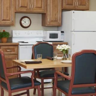 A cozy kitchen with a dining table and four chairs, featuring wooden cabinets, a refrigerator, microwave, and a decorative vase of flowers on the table.