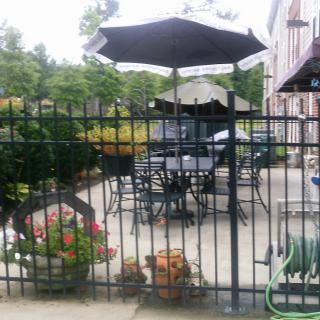 A cozy outdoor patio area with tables, chairs, and umbrellas surrounded by a fence and greenery.