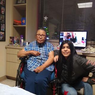 A young woman poses joyfully with an elderly man in a wheelchair, showcasing the bond of family in a hospital setting.