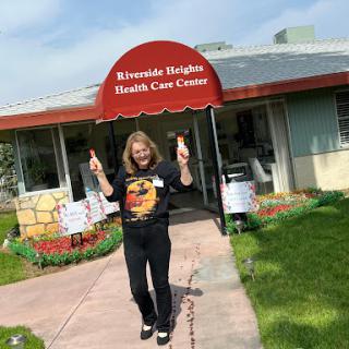 A cheerful individual poses in front of the Riverside Heights Health Care Center, enjoying a sunny day.