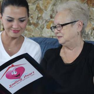 An elderly woman and a young woman sit together, reading a booklet labeled 'Smiling Faces Senior Care.'