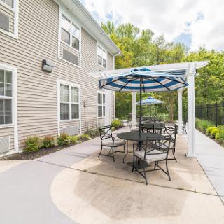 A cozy outdoor patio area featuring a table and chairs under a stylish umbrella, surrounded by lush greenery.