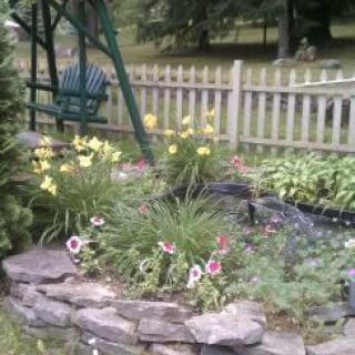 A beautiful garden with colorful flowers and a green swing next to a wooden fence.