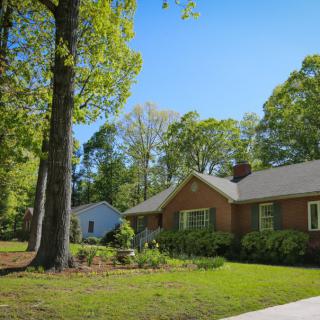 A charming suburban brick house with a lush green lawn and large trees.