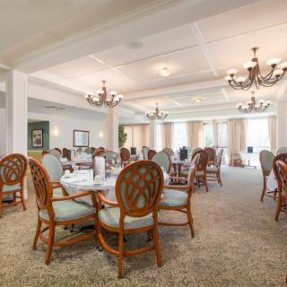 An elegant dining room with tables and chairs, illuminated by chandeliers.