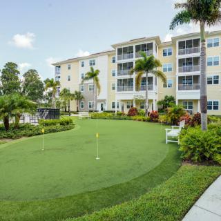 A modern residential building with a landscaped garden and putting green under a clear sky.