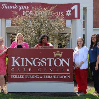 A group of people standing outside near a sign for Kingston Care Center, Skilled Nursing & Rehabilitation.