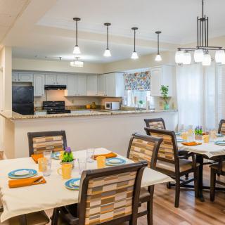 A modern dining area with neatly set tables and a view into the adjacent kitchen.