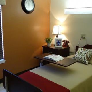 A cozy bedroom with a single bed and a bedside lamp, featuring an orange accent wall and window blinds.