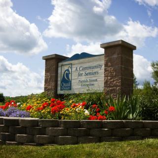 A community entrance sign surrounded by vibrant flowers under a partly cloudy sky.