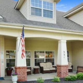 A cozy front porch of a house featuring outdoor seating and an American flag.
