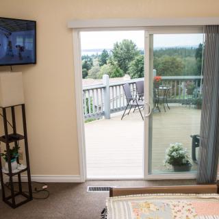 A cozy bedroom with a sliding glass door leading to a balcony overlooking nature, featuring a mounted television and simple decor.