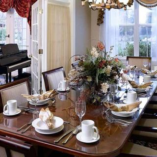 An elegantly set dining table with a floral centerpiece and a piano in the background.