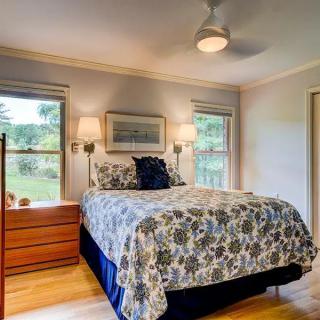 A cozy bedroom with a floral-patterned bedspread, wooden furniture, and ample natural light from two windows.