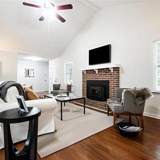 A modern living room featuring a cozy sofa, armchairs, and a brick fireplace beneath a wall-mounted TV.