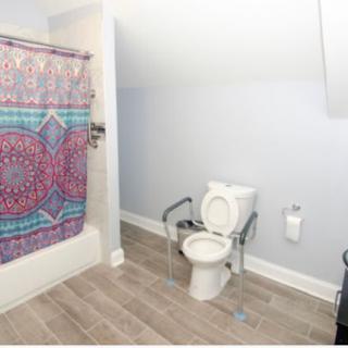 A bathroom with a toilet equipped with handrails, a bathtub, and a colorful shower curtain.