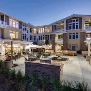 A modern apartment building with a well-lit outdoor courtyard featuring patio seating and landscaping.