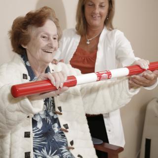 An elderly woman engaging in physical therapy with the assistance of a caregiver.