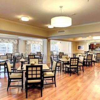 A spacious and elegant dining room with neatly arranged tables and chairs, featuring warm lighting and wooden floors.