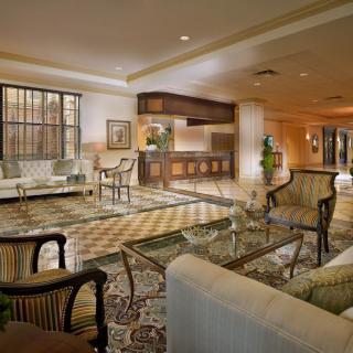 A luxurious hotel lobby featuring a reception desk, comfortable seating areas with armchairs and glass tables, and elegant decor.