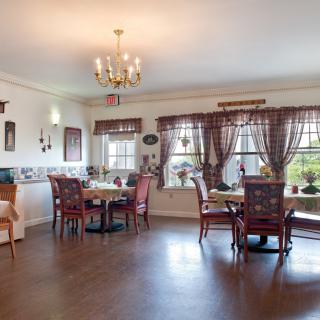 A cozy dining area with elegant lighting, wood flooring, and a view through large windows adorned with curtains.
