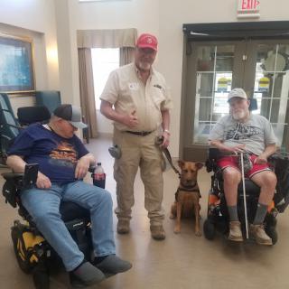 A group of individuals in wheelchairs alongside a service dog, enjoying a moment together indoors.