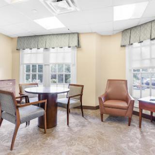 A cozy waiting area featuring a round table and comfortable seating, illuminated by natural light.