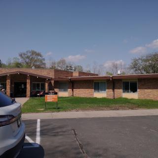A view of a brick building surrounded by green grass and trees on a sunny day.