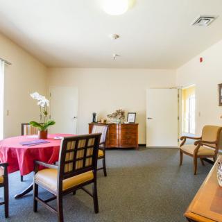 A spacious, well-lit room with a table and chairs, decorated with potted plants and elegant furniture.