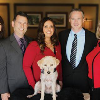A group of people in formal attire pose for a photo with a dog.