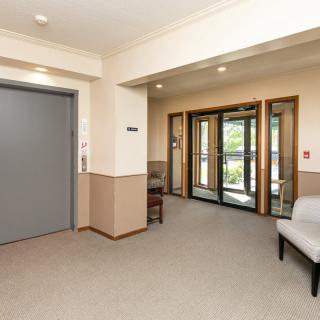 A lobby area featuring an elevator, glass entrance doors, and a seating area.