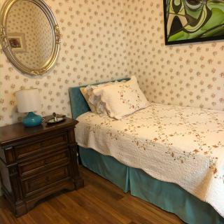A vintage-styled bedroom with a single bed, ornate nightstand, and floral wallpaper.
