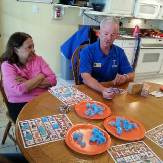 Two people playing bingo at a kitchen table with cards and plates of dough.