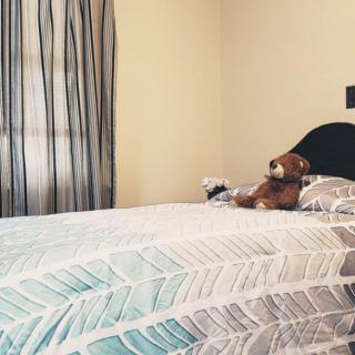 A cozy bedroom featuring a neatly made bed with a teddy bear and pillows, accompanied by elegant curtains.
