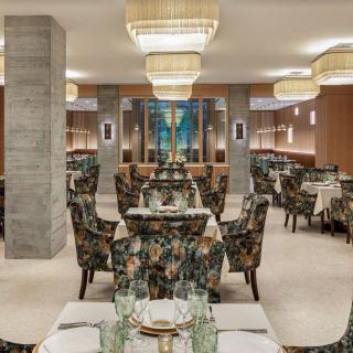 A stylish restaurant interior featuring elegant chandeliers, patterned seating, and neatly set tables.
