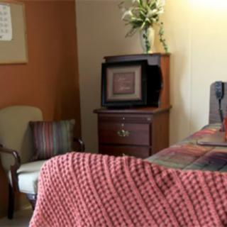 A cozy bedroom with a television, armchair, and patterned bedspread.