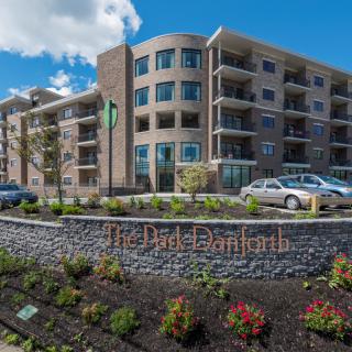A modern apartment building with well-maintained landscaping and cars parked in front.