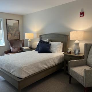 A cozy and well-lit bedroom featuring a bed with decorative pillows, bedside lamps, and comfortable seating.