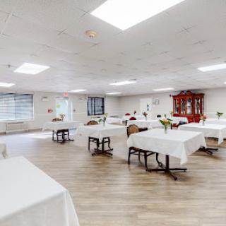 A spacious event room set up with white tablecloths and wooden flooring, ready for gatherings or meetings.