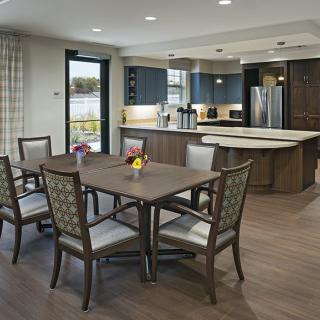 A modern kitchen with a dining area featuring a wooden table and chairs on wood flooring.