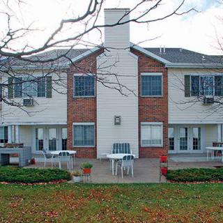 A two-story residential building with a shared patio and outdoor furniture in front.