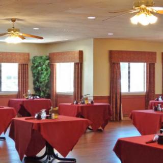 An empty restaurant dining room with tables covered in red tablecloths.