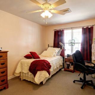 A cozy bedroom with a single bed, a desk chair, and a window with curtains.