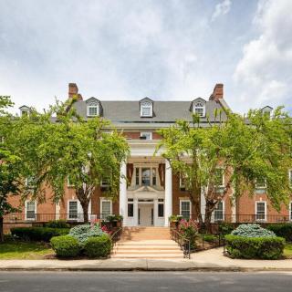 A large colonial-style residential building with a prominent front entrance, flanked by trees.
